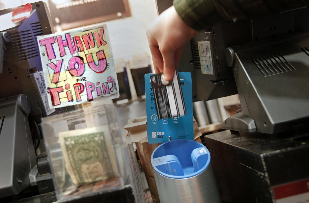 A man demonstrates the use of a DipJar, an electronic version of the tip jar found in coffee shops, on the counter of an Oren's Daily Roast in New York February 13, 2013. With a quick dip of their credit cards into the sleek machine, grateful customers are able to leave a pre-set tip (generally $1) for baristas. DipJar, a tip jar that takes plastic, located in six stores, is just one high-tech innovation seeking to make up for declining gratuities as people pay for small purchases with credit or debit cards. Picture taken February 13. To match Your Money RETAIL-SERVICE/DIPJAR                      REUTERS/Carlo Allegri  (UNITED STATES - Tags: BUSINESS SCIENCE TECHNOLOGY)