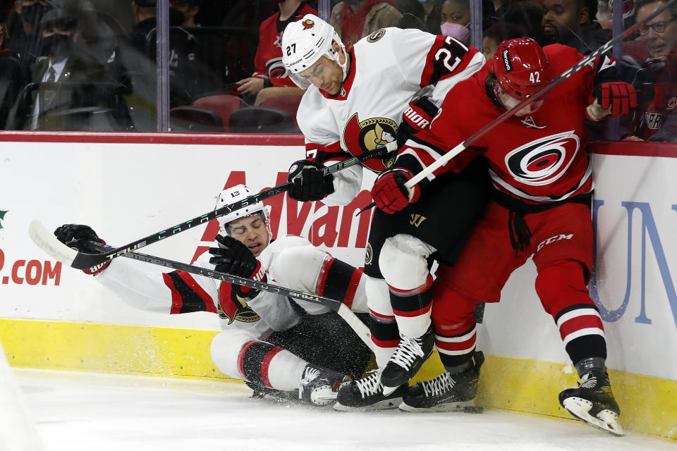 Ottawa Senators' Zach Sanford (13) joins teammate Dylan Gambrell (27) in vying for the puck against Carolina Hurricanes' Maxime Lajoie (42) during the first period of an NHL hockey game in Raleigh, N.C., Thursday, Dec. 2, 2021. (AP Photo/Karl B DeBlaker)