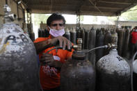 A worker refills medical oxygen cylinders at a charging station on the outskirts of Prayagraj, India, Friday, April 23, 2021. India put oxygen tankers on special express trains as major hospitals in New Delhi on Friday begged on social media for more supplies to save COVID-19 patients who are struggling to breathe. India's underfunded health system is tattering as the world's worst coronavirus surge wears out the nation, which set another global record in daily infections for a second straight day with 332,730. (AP Photo/Rajesh Kumar Singh)