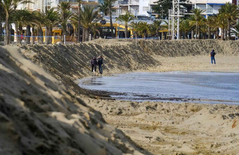 People walk past a huge sand shaft built to to protect the Arenal Beach ahead of the upcoming storm "Gloria", in Javea near Alicante