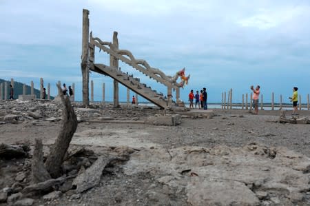 People walk and take pictures at the ruins of a Buddhist temple which has resurfaced in a dried-up dam due to drought, in Lopburi, Thailand