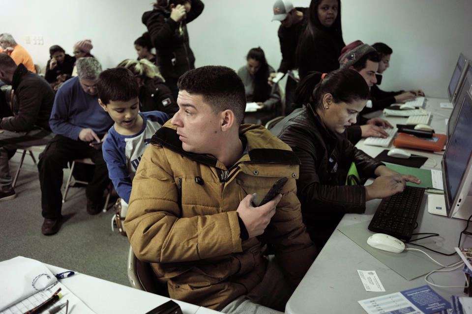 In this Wednesday, Dec. 4, 2019 photo Helison Alvarenga, of Brazil, front, sits with his 6-year-old son, David, left, and 24-year-old wife, Amanda, right, as they use a computer monitor while pursuing replacement passports at the New England Community Center, in Stoughton, Mass. Alvarenga, a 26-year-old from the Brazilian state of Minas Gerais, arrived in Massachusetts about four months ago after crossing the Mexican border at Juarez with his family. The three were at the community center Dec. 4, to apply for new Brazilian passports, which Alvarenga says were seized by border officials. (AP Photo/Steven Senne)