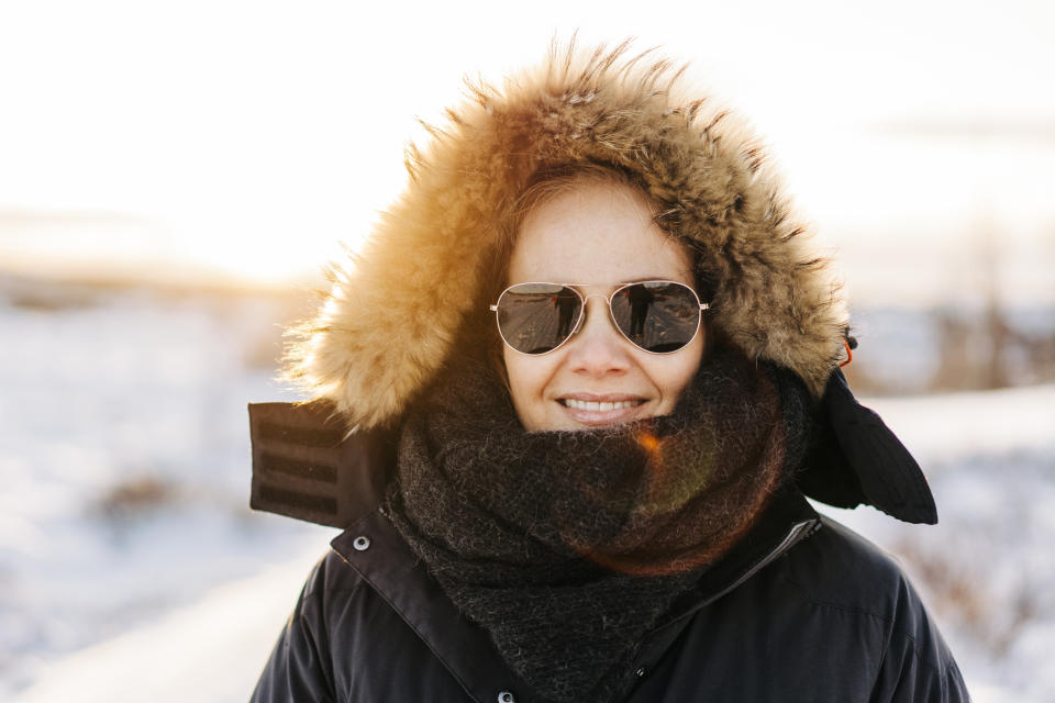 Mature woman outside in winter with sun shining and sunglasses on with fur hood up