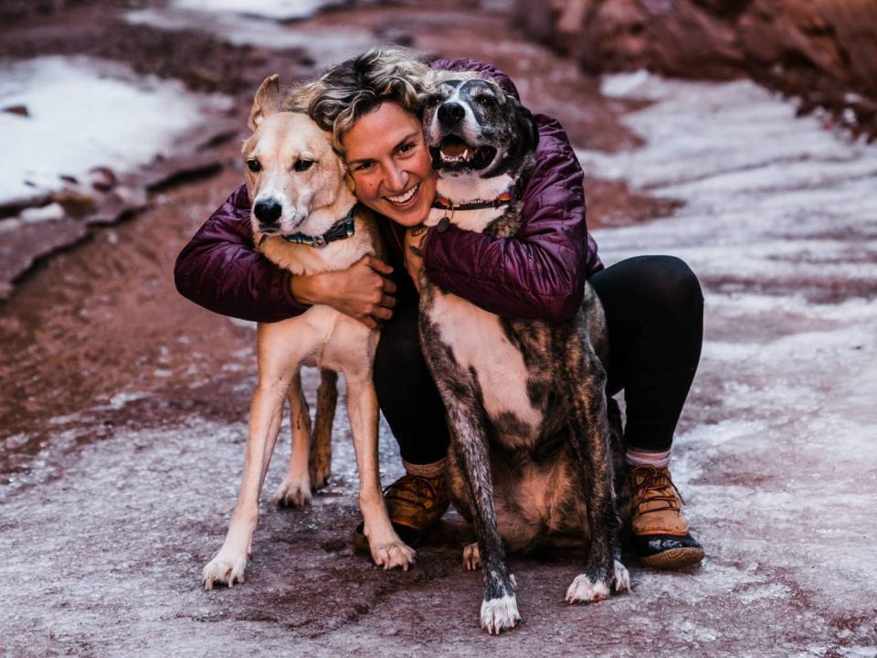 Madia hugging two of her dogs while out in nature.