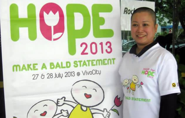 A lady posing beside a Hair for Hope banner. (Hair for Hope Facebook Photo)