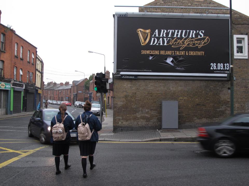 Morning commuters and two schoolgirls pass a billboard advertising Arthur's Day in Dublin, Ireland, on Thursday, Sept. 26, 2013. Ireland's love affair with pub and pint is sparking national soul-searching as never before because of an unofficial holiday dreamed up by Guinness. Thursday's celebrations of Arthur's Day, honoring the 18th-century founder of Ireland's quintessential drink, feature surprise musical performances in 815 pubs and clubs across Ireland as well as concerts worldwide from Malaysia to Jamaica. (AP Photo/Shawn Pogatchnik)