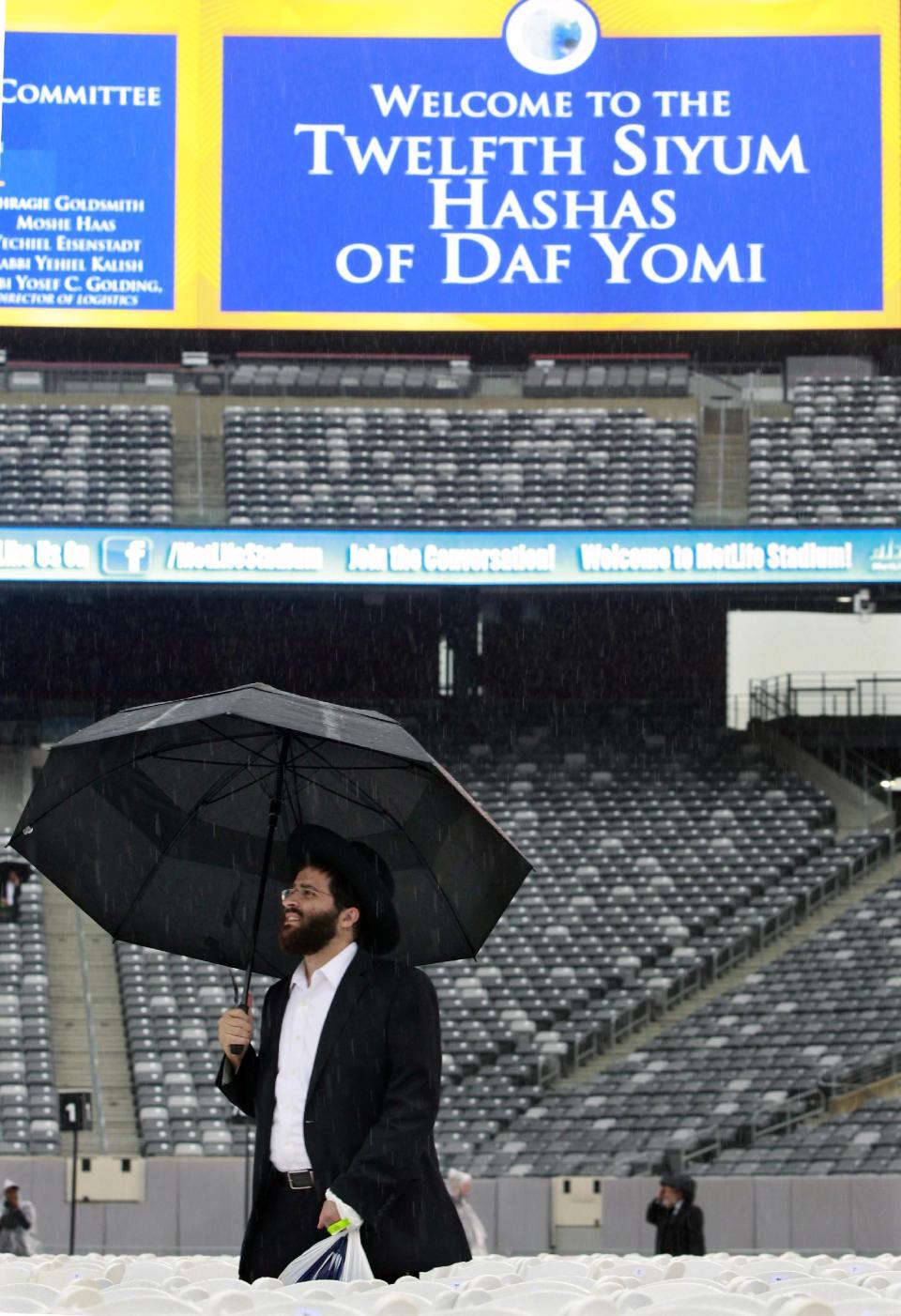 A man walks in the rain at MetLife stadium in East Rutherford, N.J, Wednesday, Aug. 1, 2012, as he waits for the start of the celebration Siyum HaShas. The Siyum HaShas, marks the completion of the Daf Yomi, or daily reading and study of one page of the 2,711 page book. The cycle takes about 7½ years to finish. This is the 12th put on my Agudath Israel of America, an Orthodox Jewish organization based in New York. Organizers say this year's will be, by far, the largest one yet. More than 90,000 tickets have been sold, and faithful will gather at about 100 locations worldwide to watch the celebration. (AP Photo/Mel Evans)