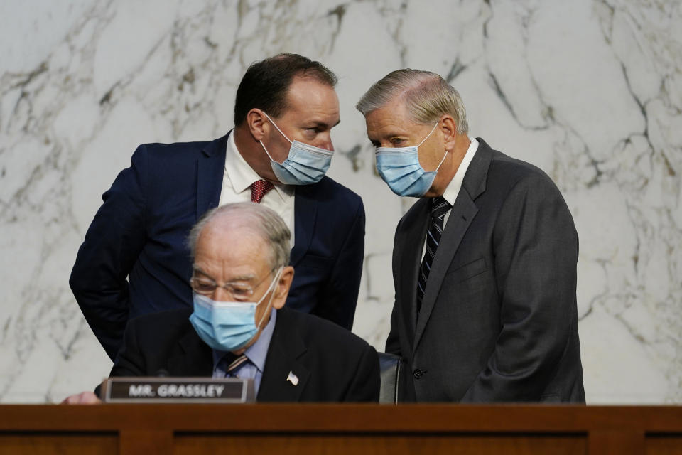 Senate Judiciary Committee Chairman Sen. Lindsey Graham, standing right, talks to Sen. Mike Lee, R-Utah., as Sen. Charles Grassley, R-Iowa, sits below, before a confirmation hearing for Supreme Court nominee Amy Coney Barrett before the Senate Judiciary Committee, Monday, Oct. 12, 2020, on Capitol Hill in Washington. (AP Photo/Susan Walsh, Pool)