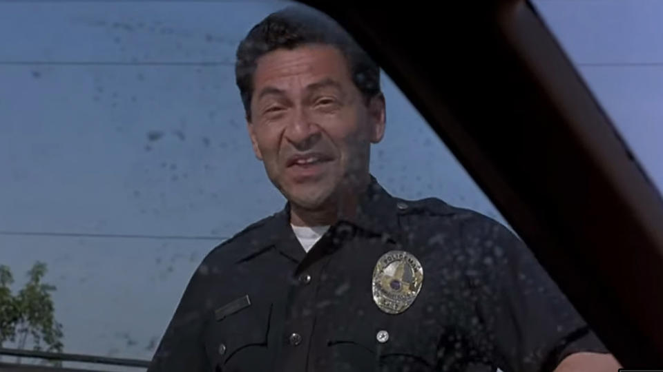 Mike Gomez smiling and laughing, as a cop, in the Big Lebowski