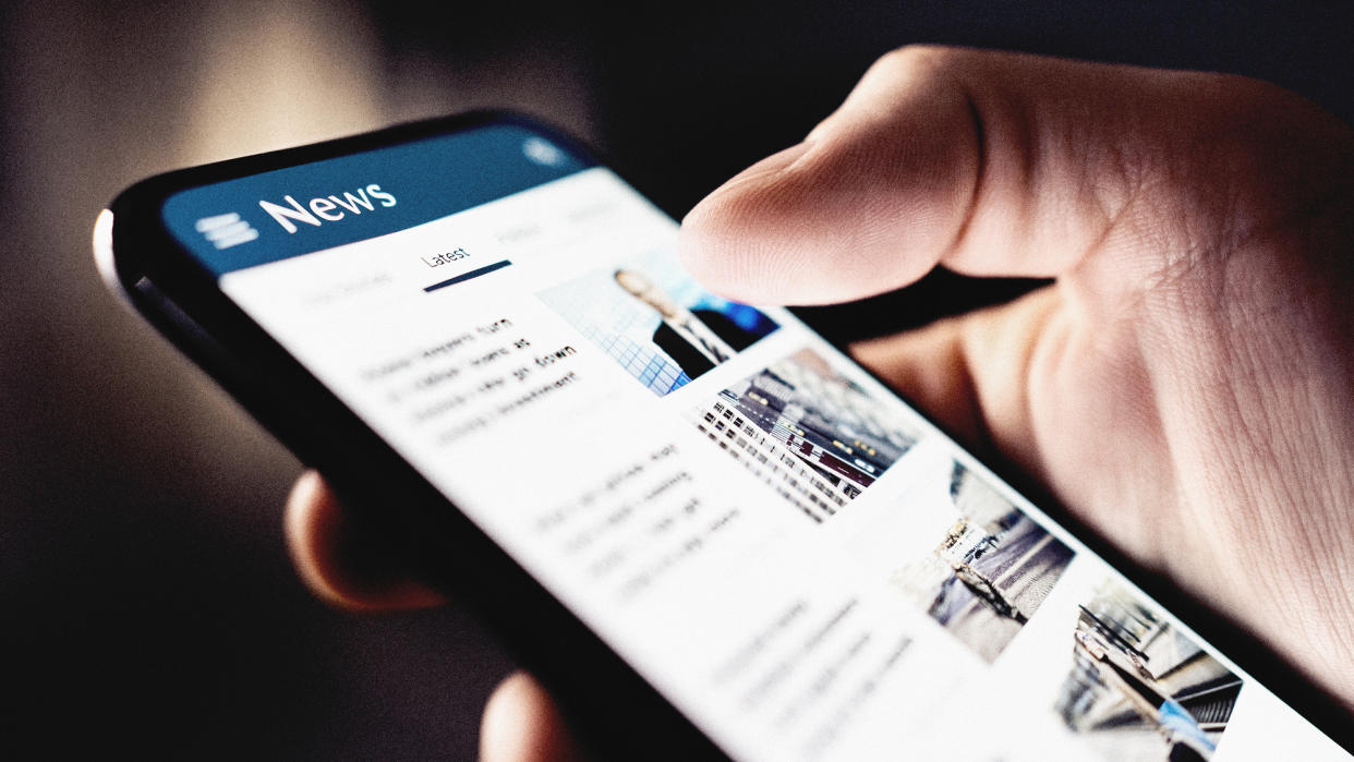  Close-up of a hand looking at news on a smartphone. 