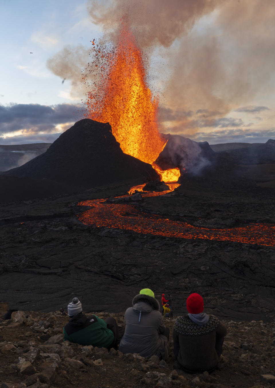 People watch as lava flows from an eruption of the Fagradalsfjall volcano on the Reykjanes Peninsula in southwestern Iceland on Tuesday, May 11, 2021. The glow from the bubbling hot lava spewing out of the Fagradalsfjall volcano can be seen from the outskirts of Iceland's capital, Reykjavík, which is about 32 kilometers (20 miles) away. (AP Photo/Miguel Morenatti)