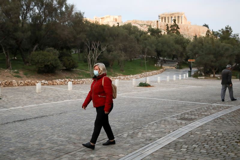 FILE PHOTO: A woman wearing a protective mask walks down a pedestrian street near the Parthenon, amid the coronavirus disease (COVID-19) pandemic, in Athens