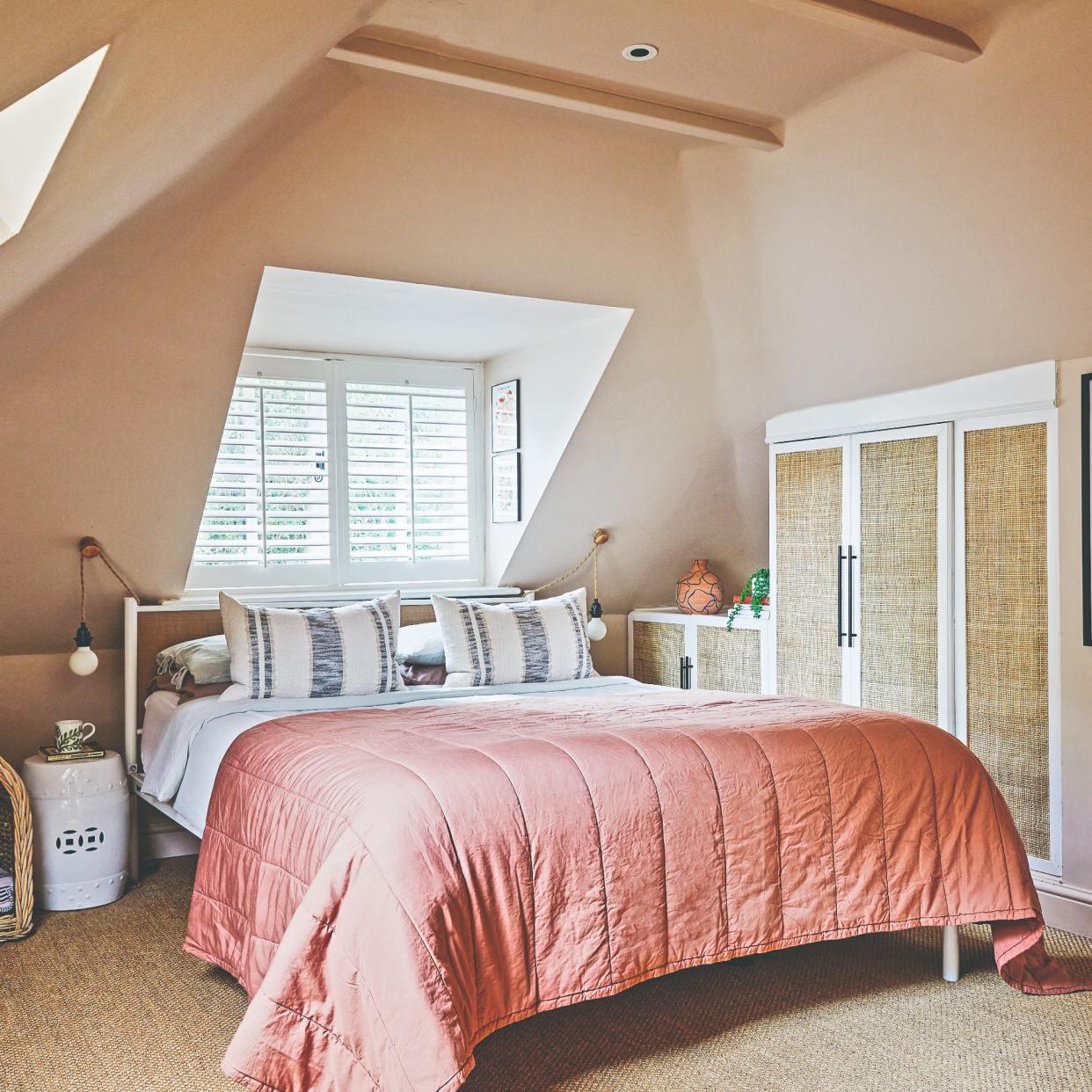  A peach-painted attic bedroom with a tonal bedspread on the bed and downlights at the ceiling. 