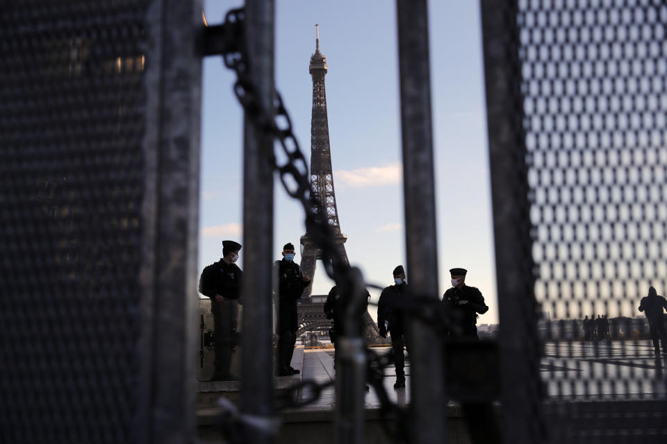 Policemen stand guard behind a security fence during a protest against bill on police images, in Paris, Saturday, Nov. 21, 2020. Thousands of people took to the streets in Paris and other French cities Saturday to protest a proposed security law they say would impinge on freedom of information and media rights. The Eiffel tower is seen background. (AP Photo/Christophe Ena)