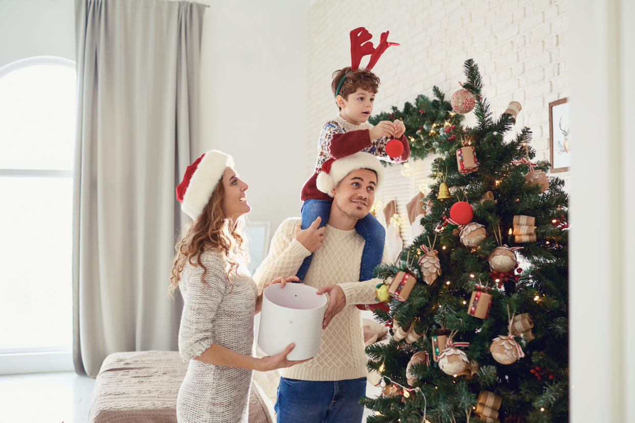 Mother, father and son in sweaters paint the Christmas tree in the house.