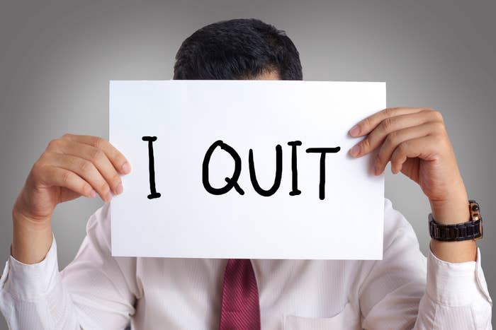 Person holding a sign that reads "I QUIT" in front of their face, indicating resignation from a job