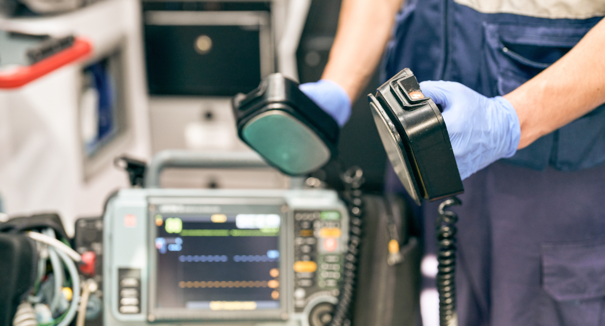 paramedic wearing gloves holding defibrillator in hands wearing gloves helping patient with heart attack, widow-maker heart attack 