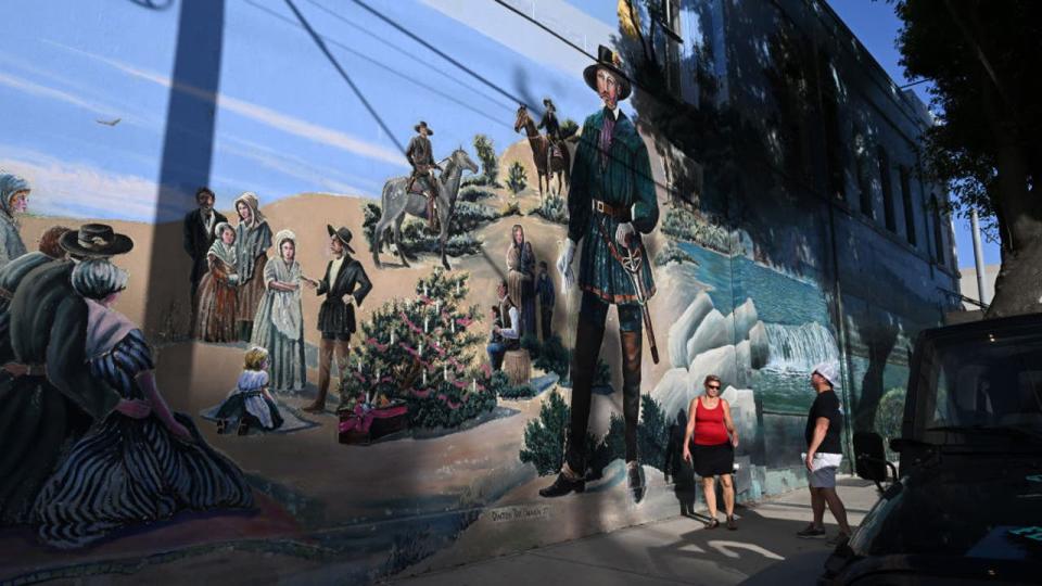 <div>NEW BRAUNFELS, TX - JULY 29: People walk by a mural that depicts the town's early German settlers on Saturday July 29, 2023 in New Braunfels, TX. Guns are a daily way of life for many Texans. (Photo by Matt McClain/The Washington Post via Getty Images)</div>