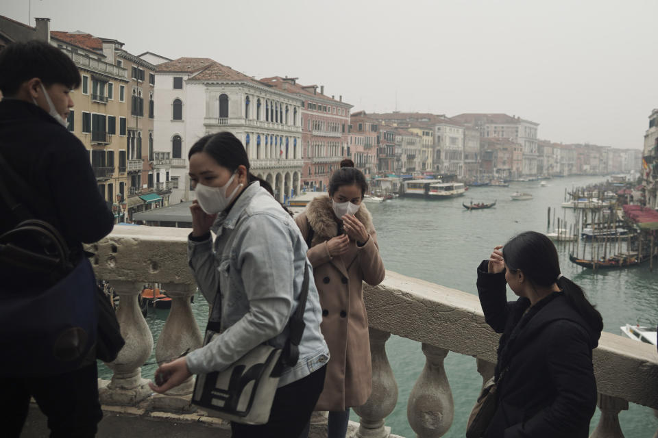 FILE - In this Feb. 25, 2020 file photo, tourists fiddle with their protective face masks as they take selfies atop Rialto bridge in Venice, Italy. Still reeling from the effects of major flooding just a few months ago, Venice faces a new emergency: the threat of a new virus outbreak across Italy that is scaring international visitors world-wide and hitting the economy hard. (AP Photo/Renata Brito)