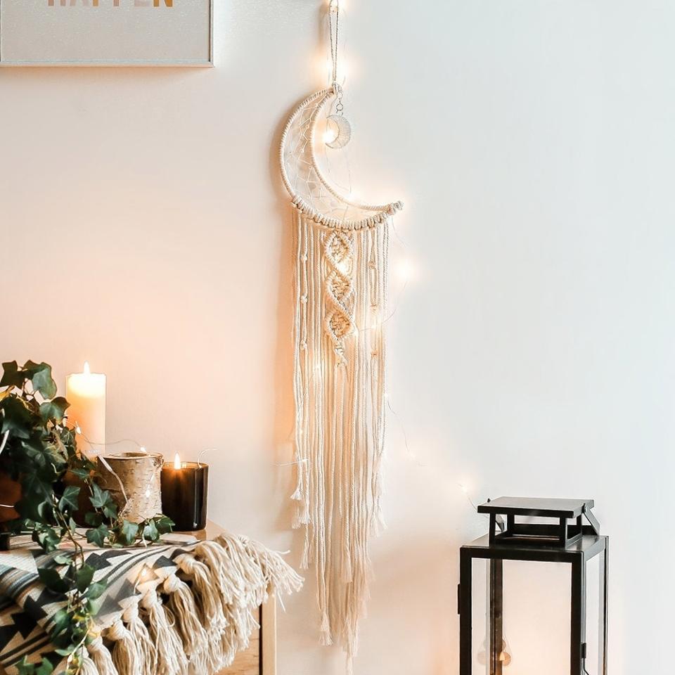 Wall-mounted moon macrame art piece with tassels, near a cozy home decor setup