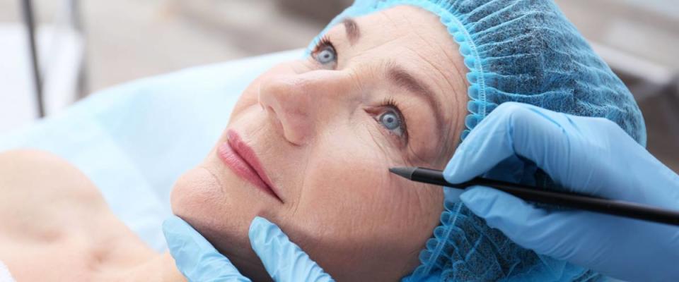 Surgeon hand drawing marks on female face for plastic operation