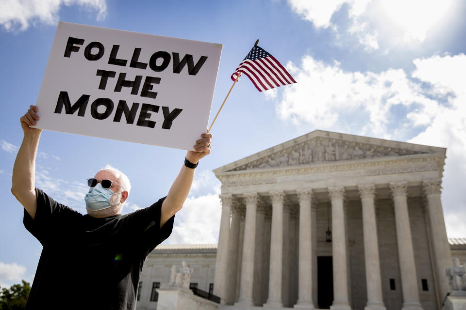 FILE - In this Thursday, July 9, 2020, file photo, Bill Christeson holds up a sign that reads "Follow the Money" outside the Supreme Court in Washington after it ruled that President Donald Trump must release his tax records. Trump's lawyers filed fresh arguments Monday, July 27, to try to block or severely limit a criminal subpoena for his tax records, calling it a harassment of the president. (AP Photo/Andrew Harnik, File)