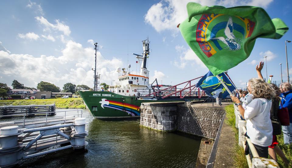 A woman holds a Greenpeace flag and waves as Greenpeace’s Dutch-flagged Artic Sunrise ship returns to the Netherlands on August 9, 2014