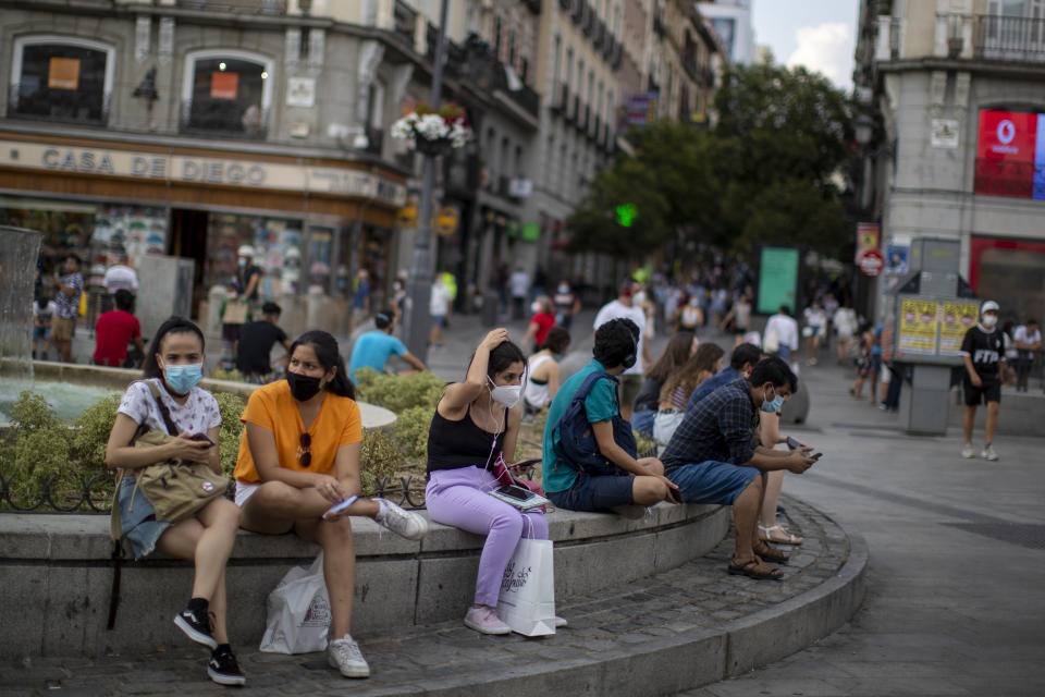 People wearing face masks to prevent the spread of coronavirus, sit on a bench street in downtown Madrid, Spain, Tuesday, July 28, 2020. The Madrid regional government is making the use of face masks mandatory in all public areas, limiting how many people can gather in one place and targeting young people in a drive to stamp out new outbreaks of COVID-19. (AP Photo/Manu Fernandez)