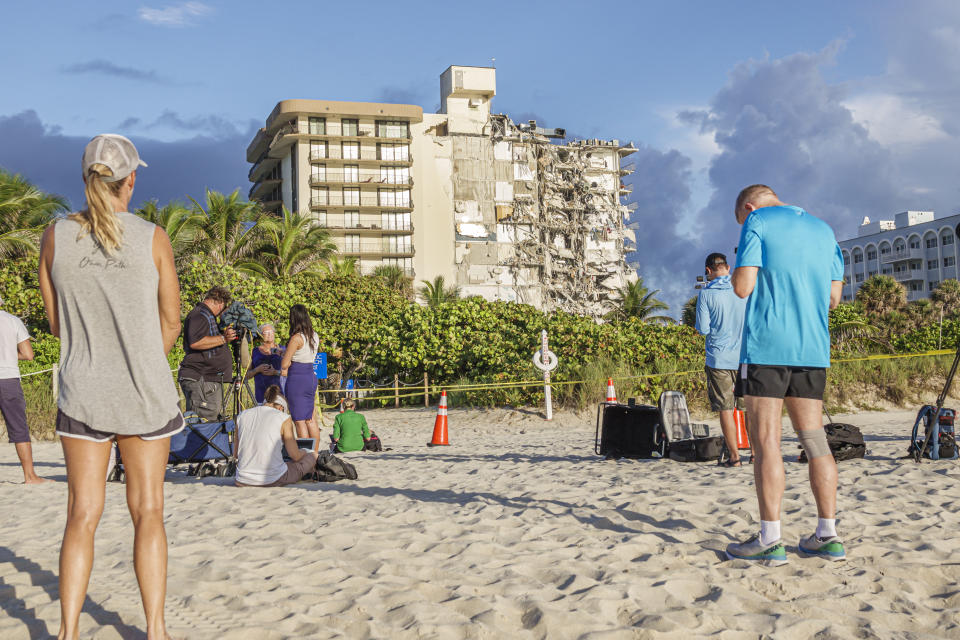 People stand on the beach looking at the collapsed Champlain Towers South in Surfside.