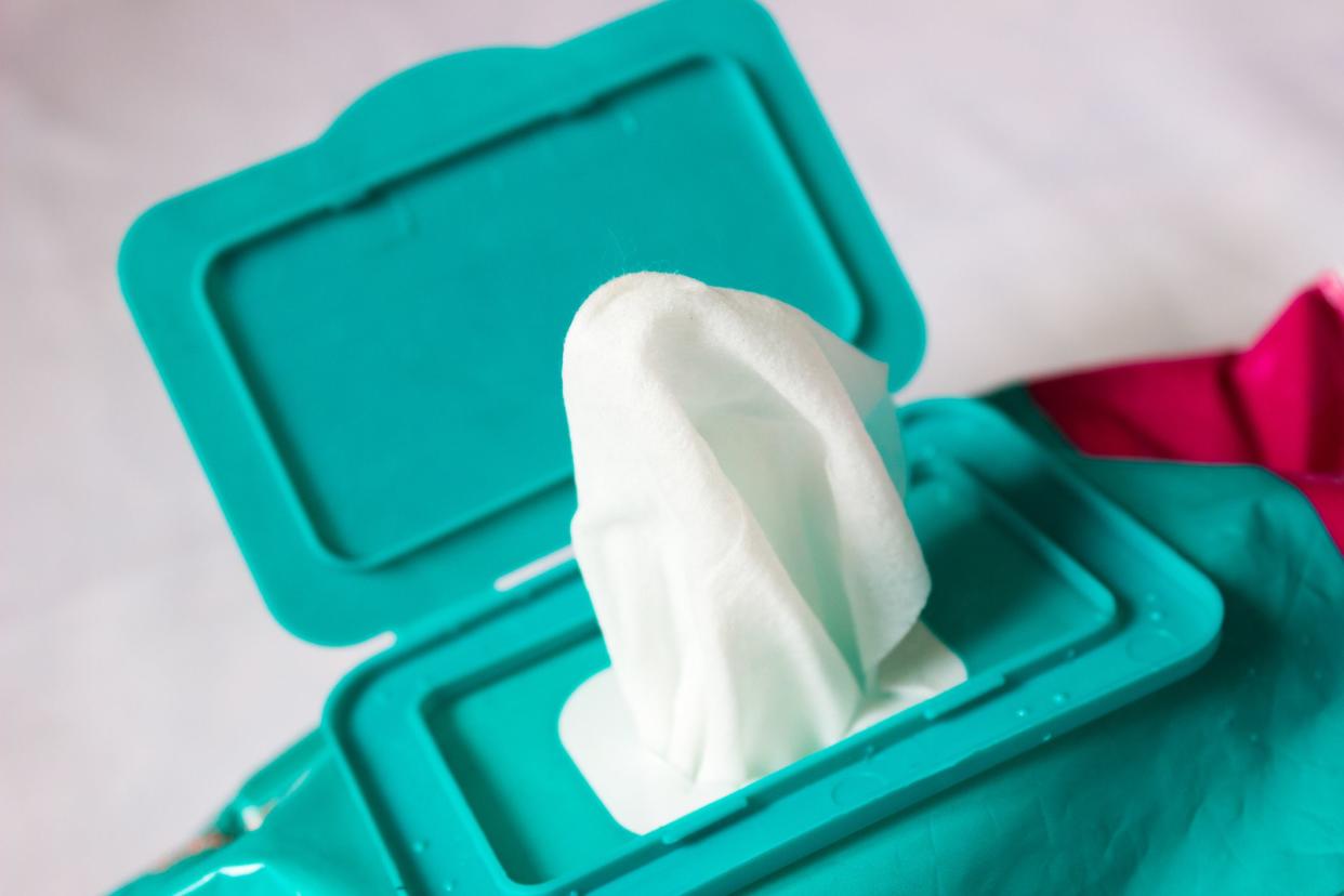 Wet wipe pulled but still attached to container, against a white background