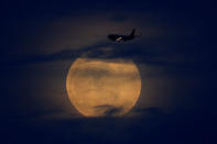 A full moon rises between clouds as a landing commercial jet approaches the airport before the start of a total lunar eclipse that is being called a 'Super Blood Wolf Moon' in San Diego, California, U.S., January 20, 2019. REUTERS/Mike Blake