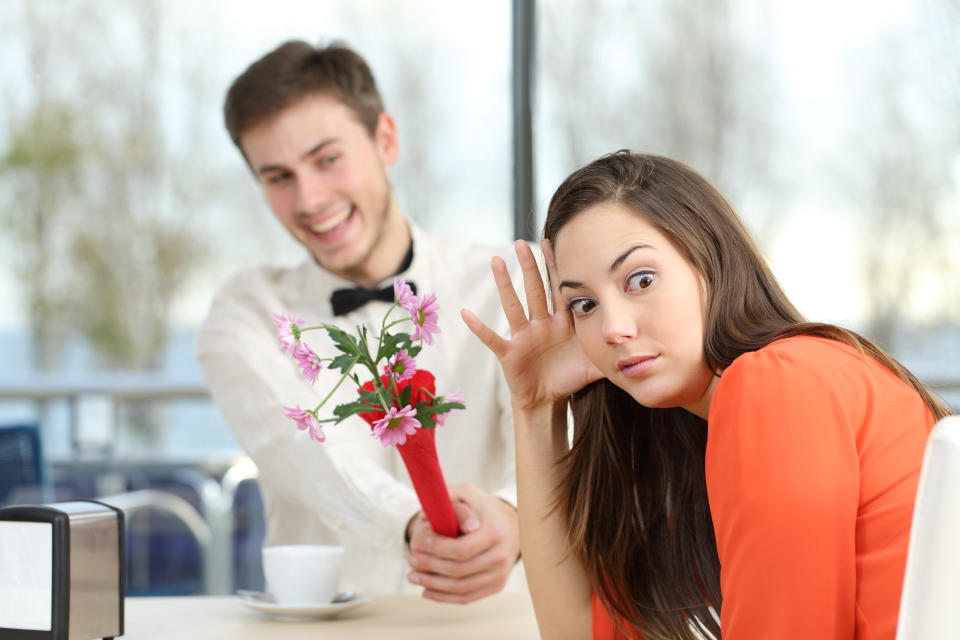 Disgusted woman rejecting a geek boy offering flowers in a blind date in a coffee shop interior