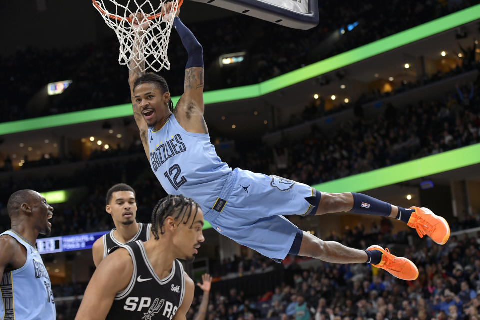 Memphis Grizzlies guard Ja Morant (12) hangs from the rim after dunking against the San Antonio Spurs in the second half of an NBA basketball game Tuesday, Jan. 2, 2024, in Memphis, Tenn. (AP Photo/Brandon Dill)