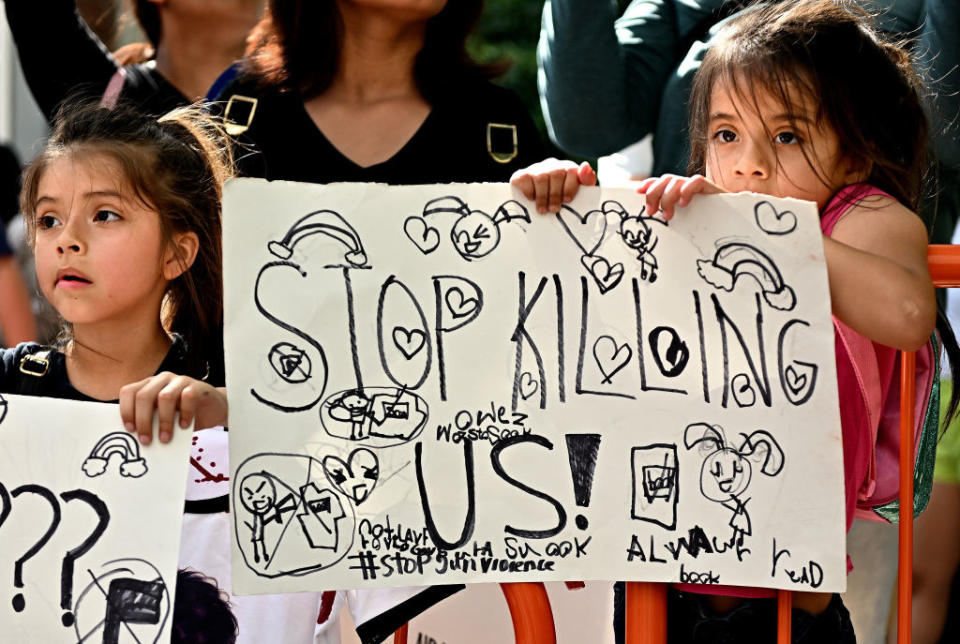 A child holds a sign that says "stop killing us"