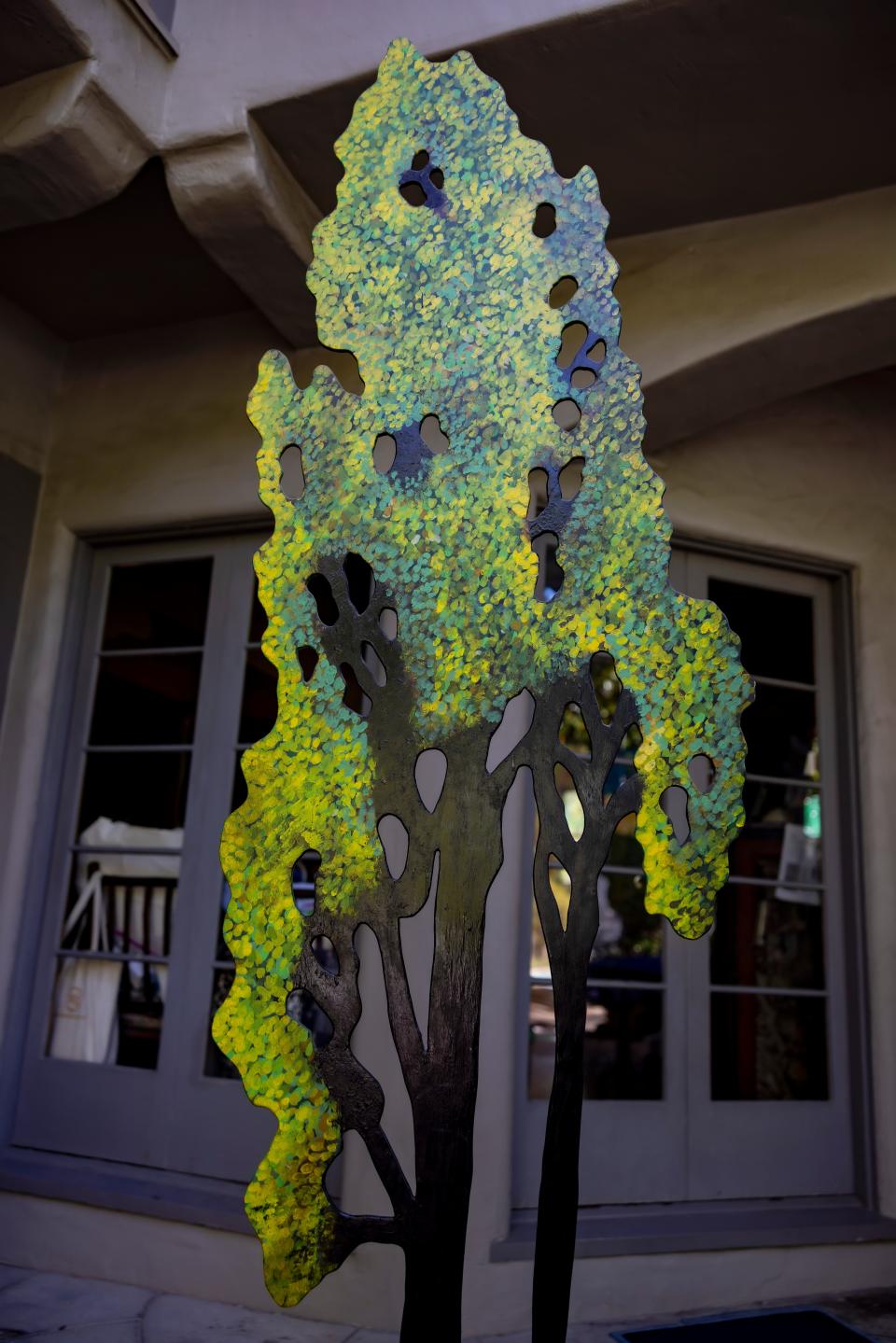 A sculpture of a tree seen with a row of windows behind it.