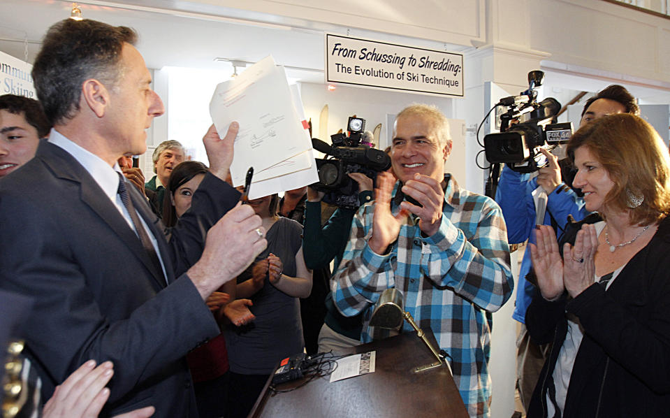 FILE - Jake Burton, the creator of Burton Snowboards, center, and his wife Donna Carpenter, right, applaud Gov. Peter Shumlin after he signed a bill in Stowe, Vt., making skiing and snowboarding the official sports of Vermont, in this March 8, 2012, file photo. A new documentary on the late snowboarding pioneer Jake Burton is more than a glossy retrospective of his life. Jake Burton had been approached about a movie of his life story and had started planning to make it. His wife, Donna, let the project move forward after Burton's death. One of her instructions to director Fernando Villena was that there was no subject that would be out of bounds.(AP Photo/Toby Talbot, File)