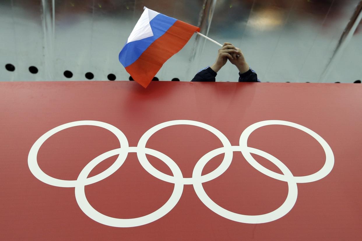 FILE - In this Feb. 18, 2014, file photo, a Russian flag is held above the Olympic Rings at Adler Arena Skating Center during the Winter Olympics in Sochi, Russia.  A World Anti-Doping Agency (WADA) panel on Monday Nov. 25, 2019, has recommended Russian athletes be forced to compete as neutrals at the 2020 Olympics in Tokyo and other major upcoming events. (AP Photo/David J. Phillip, File)