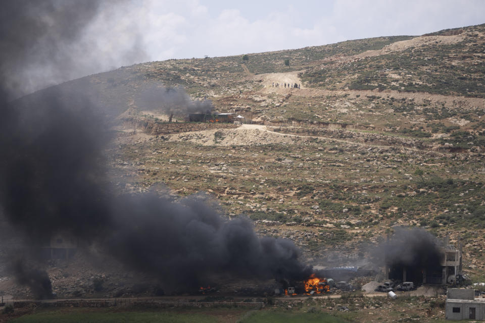 Israeli settlers gather near burning properties of Palestinian villagers after they set on fire, in the West Bank village of al-Mughayyir, Saturday, April 13, 2024. Israel's army says the body of a missing Israeli teen has been found in the occupied West Bank after he was killed in a "terrorist attack." The disappearance of 14-year-old Binyamin Achimair sparked a large attack by settlers on a Palestinian village on Friday and Saturday. (AP Photo/Nasser Nasser)