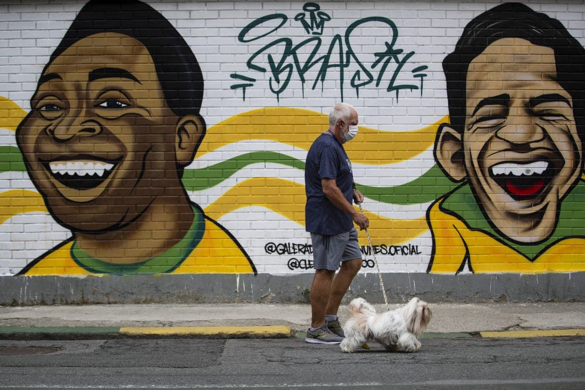 A man walks his dog past a mural of Brazilian soccer stars Pele, left, and Garrincha in Rio de Janerio, Brazil, Friday, Dec. 30, 2022. (AP Photo/Bruna Prado)