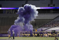 Washington players run out of a tunnel through a cloud of purple smoke in front of empty seats at Husky Stadium before an NCAA college football game against Utah, Saturday, Nov. 28, 2020, in Seattle. Due to the COVID-19 pandemic, no fans were in attendance at the game. (AP Photo/Ted S. Warren)