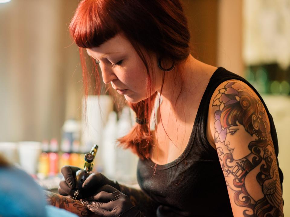 red haired tattoo artist inking a client
