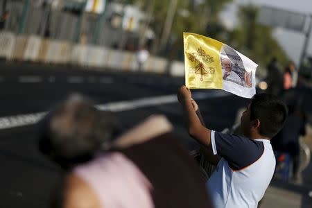 A boy waves a flag in the colors of the Vatican and a photograph of Pope Francis as he waits along with others for the pope to drive past in Mexico City, February 12, 2016. REUTERS/Carlos Garcia Rawlins