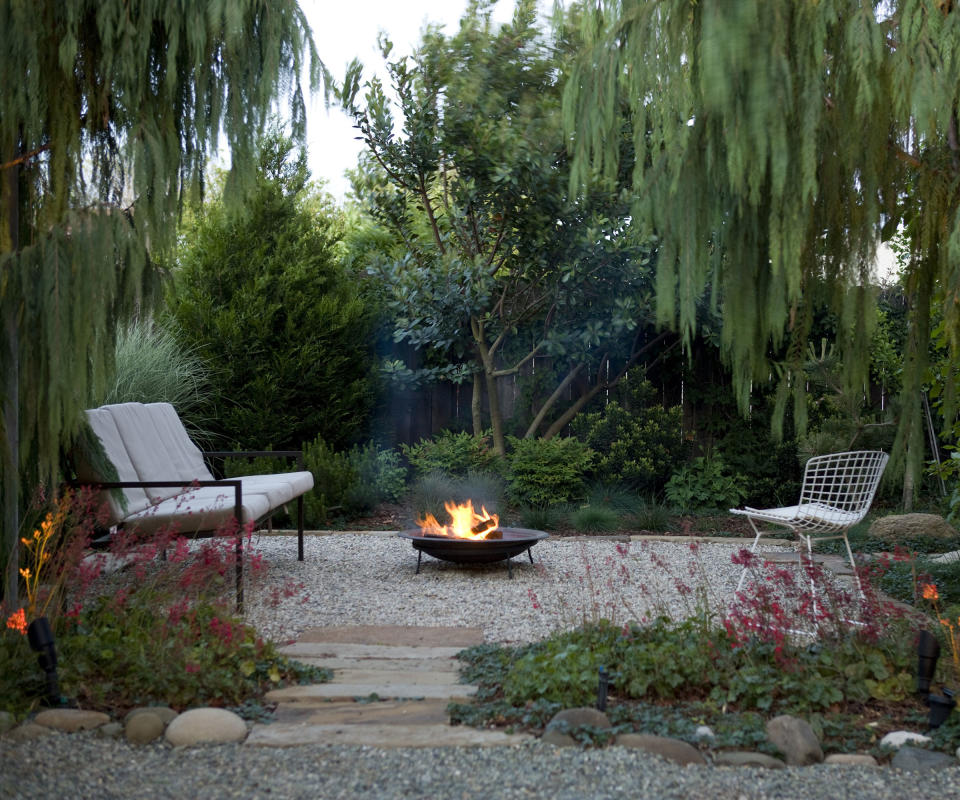 gravel patio area underneath trees with seating and a fire pit