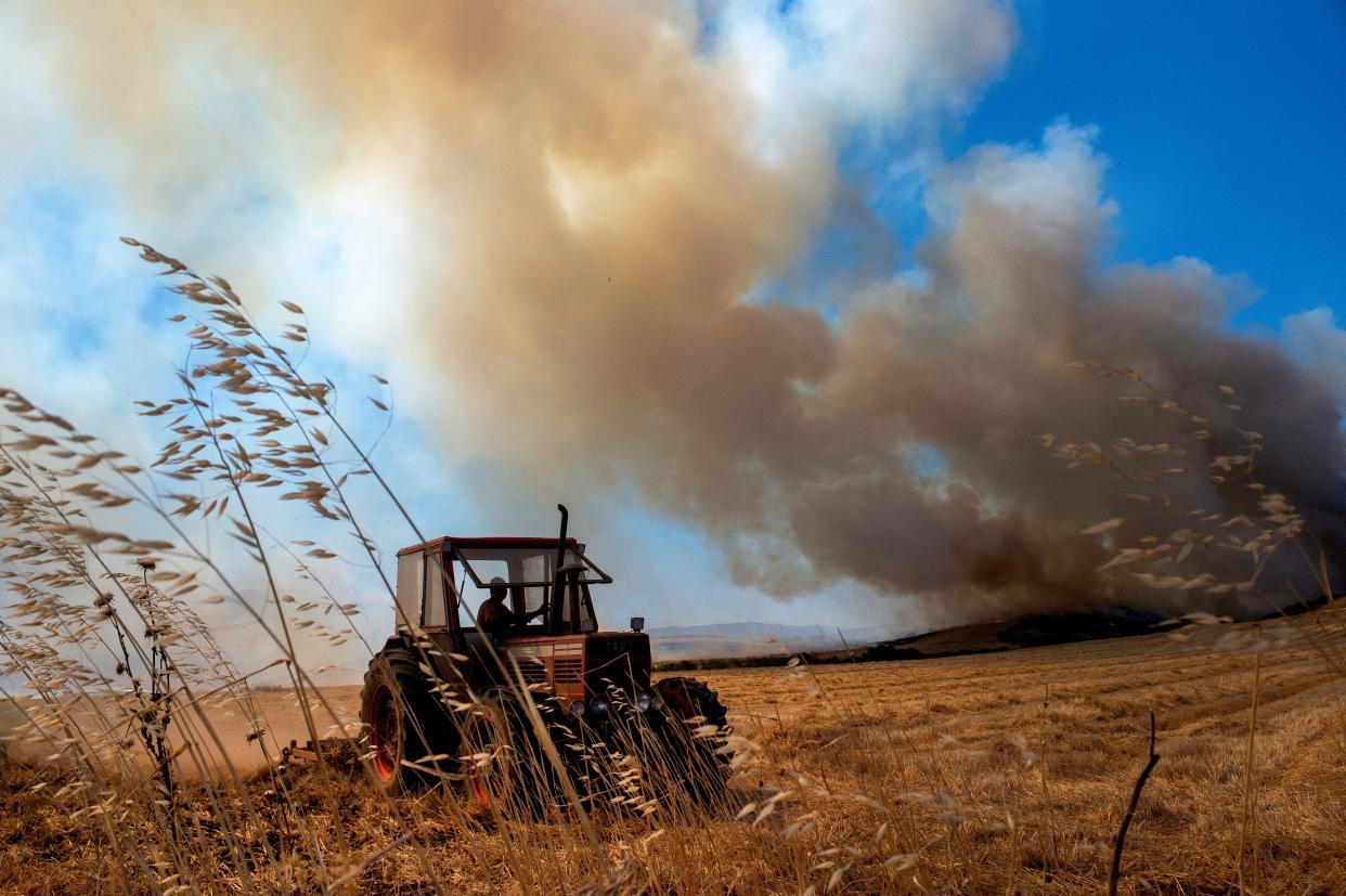 A farmer operates a tractor during a wildfire in Velestino, Magnesia prefecture (EPA)