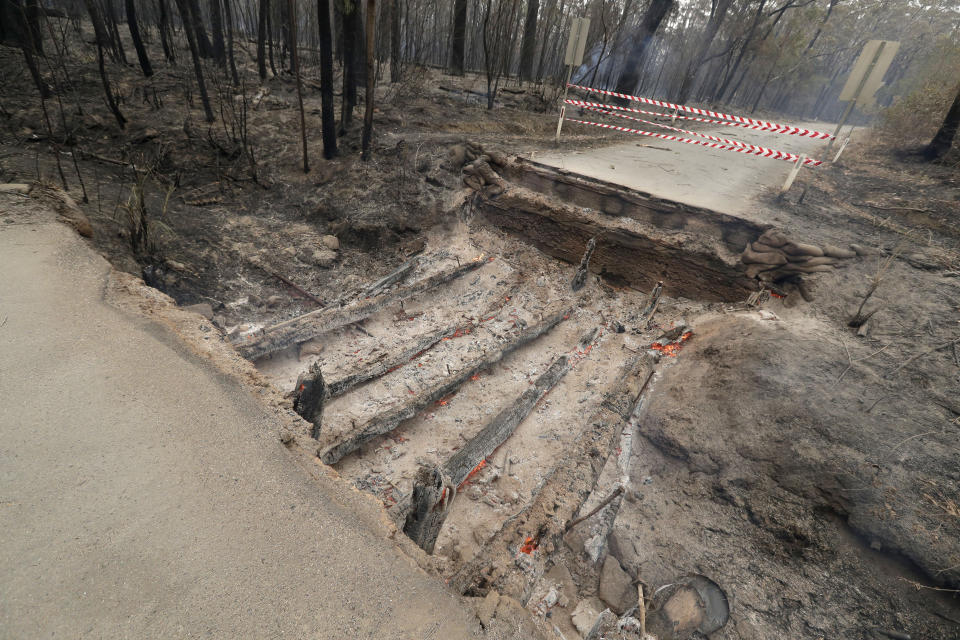 Timbers from a small bridge smolder after fire destroyed the crossing near Burrill Lake, Sunday, Jan. 5, 2020. Milder temperatures Sunday brought hope of a respite from wildfires that have ravaged three Australian states, destroying almost 2,000 homes. (AP Photo/Rick Rycroft)
