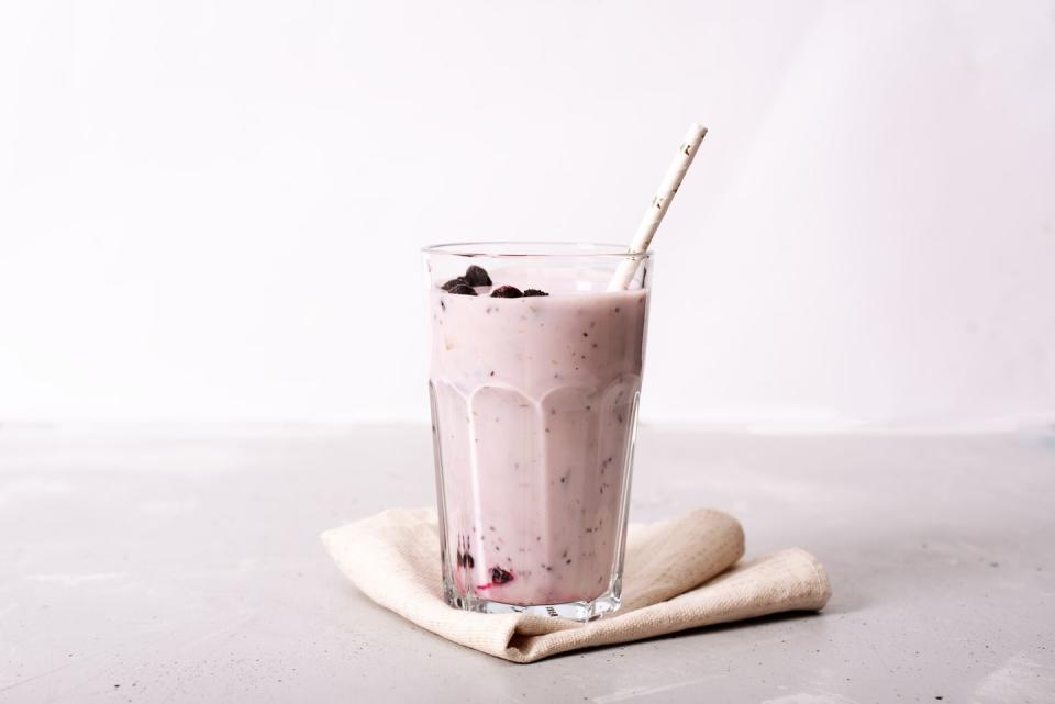 two glasses of blueberries smoothie on pink background poring from blender into glass