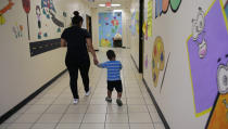 A young migrant boy walks with a Comprehensive Health Services caregiver at a "tender-age" facility for babies, children and teens, in Texas' Rio Grande Valley, Thursday, Aug. 29, 2019, in San Benito, Texas. Sheltering migrant children has become a booming business for Comprehensive Health Services, a Florida-based government contractor, as the number of children in government custody has swollen to record levels over the past two years. (AP Photo/Eric Gay)