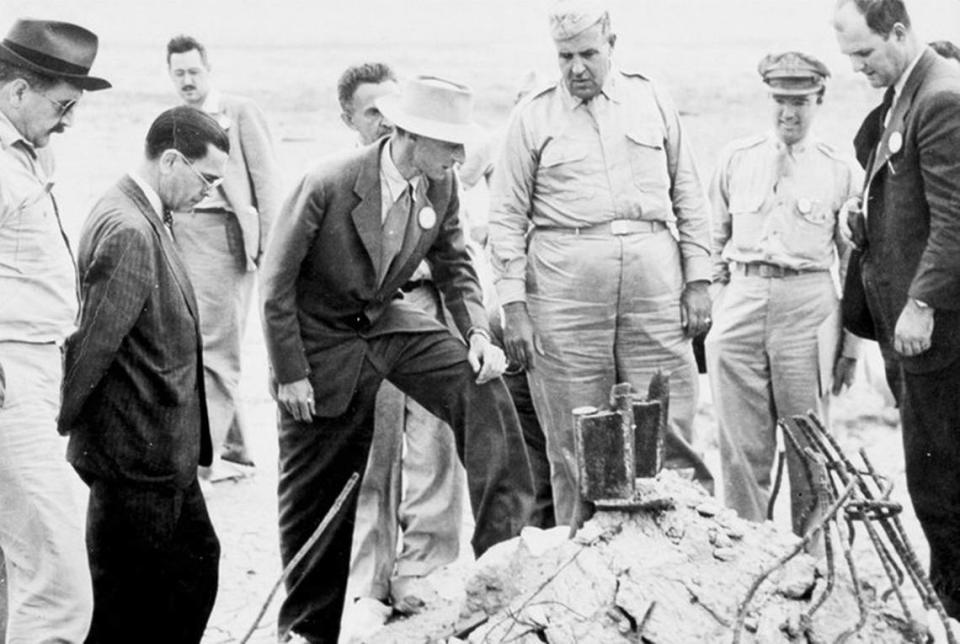 J. Robert Oppenheimer, alongside General Leslie Groves and others, inspects the aftermath of the Trinity Test in the New Mexico desert.