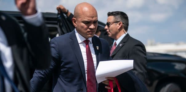 walt nauta, wearing a blue suit and red tie, walks past two men while leaving a black car on an airport tarmac