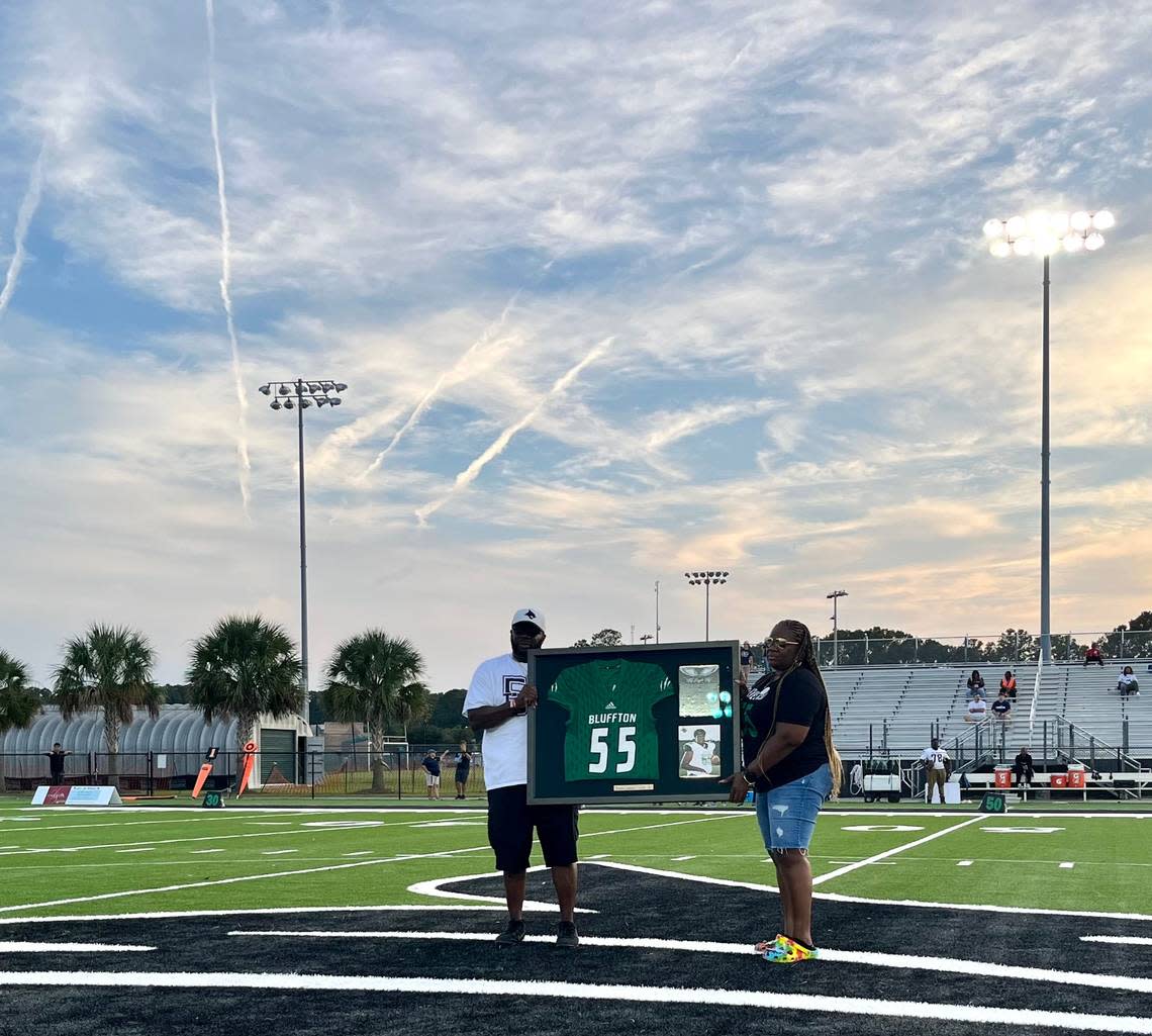 The parents of Dwon “DJ” Fields Jr., Keema Bryant and Dwon Fields, held up their son’s framed jersey at a number retirement ceremony on the school’s football field Friday that will be hung in the school’s hallway.